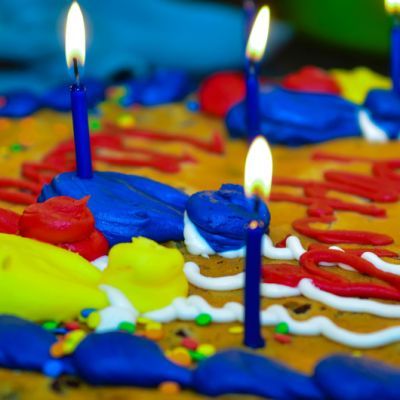 the birthday cake is decorated with blue and red icing, while three candles are lit