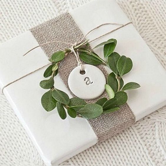 a gift wrapped in white paper and tied up with a green leaf wreath on top