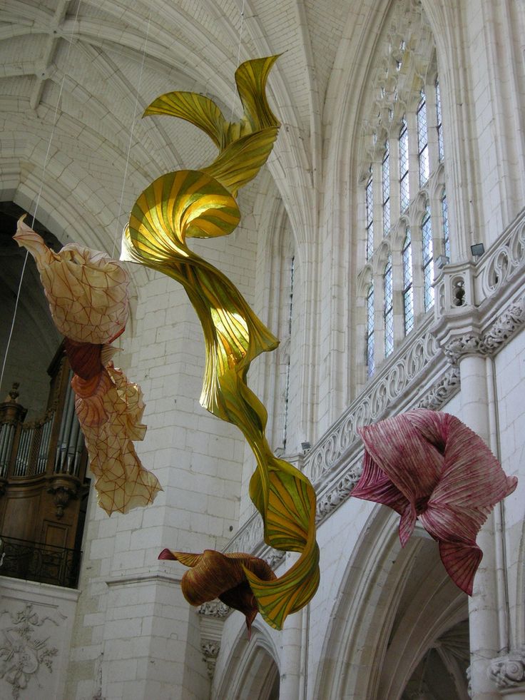 three blown glass flowers hanging from the ceiling in a cathedral like building with arched windows