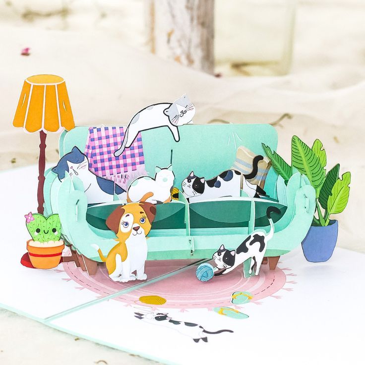 a paper model of a couch with cats and dogs on it, sitting in front of a lamp