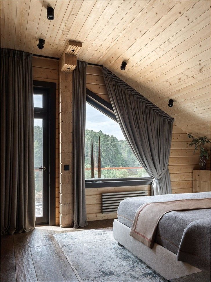 a bedroom with wood walls and flooring has a large bed in the corner near a window