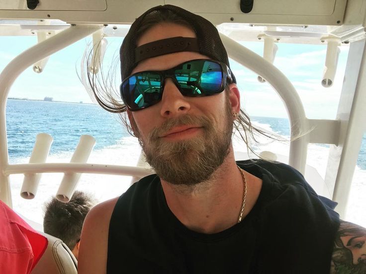 a man with sunglasses on sitting next to another man in a boat near the ocean