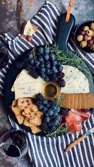 an assortment of cheeses, crackers, and grapes on a plate with wine