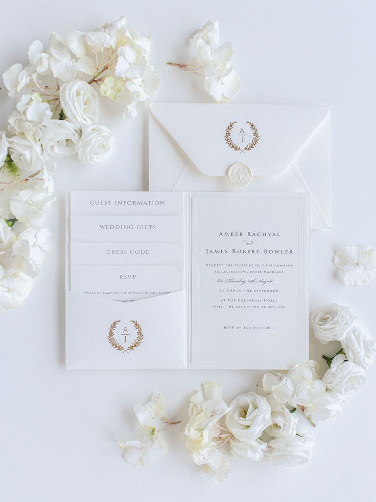 the wedding stationery is laid out on top of white flowers, and there are two rings