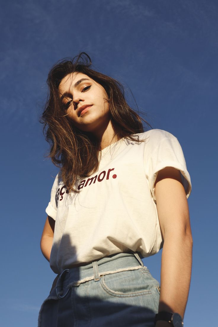 a woman standing in front of a blue sky with her hands on her hips and looking off to the side