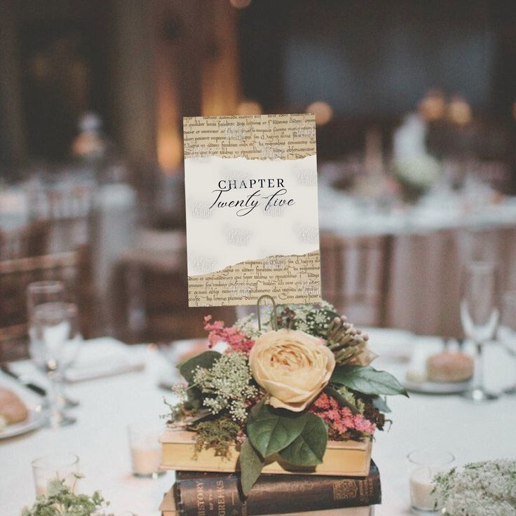 a table topped with books covered in flowers and greenery next to a white table cloth