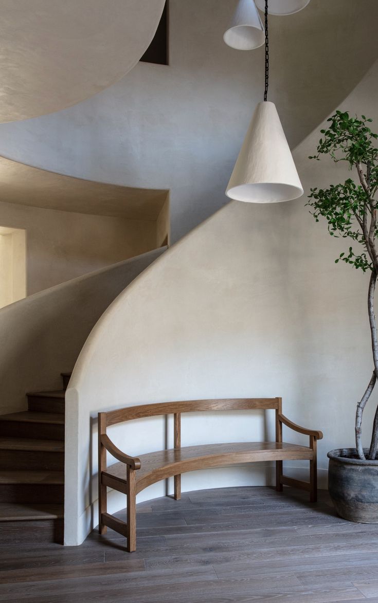 a wooden bench sitting next to a tree in a room with white walls and stairs