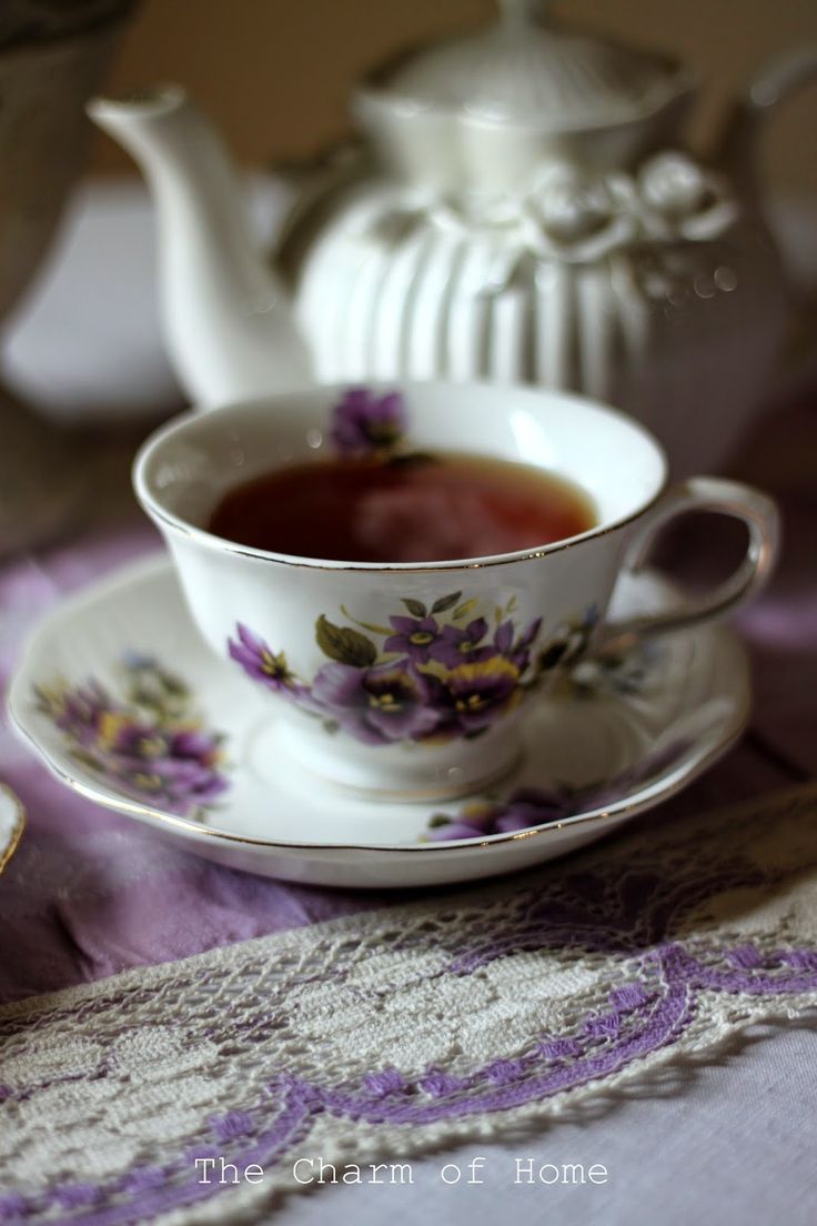 there is a tea cup and saucer on the table with purple flowers in it