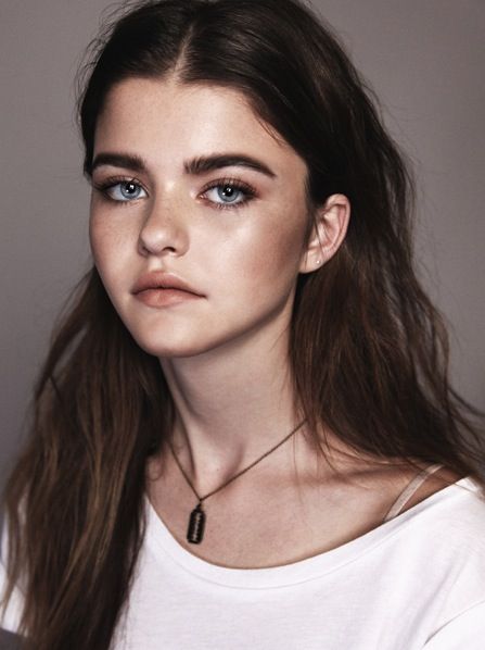 a woman with long hair and blue eyes wearing a white t - shirt is looking at the camera