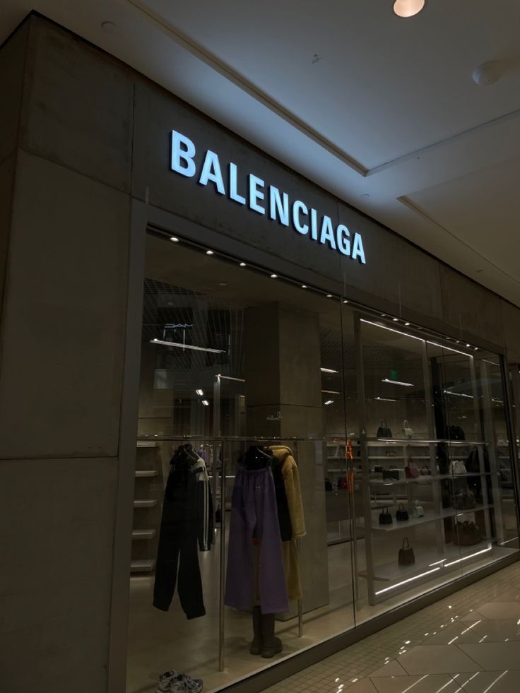 a clothing store with clothes on display in the window and lighted sign above it that says baleinicaa