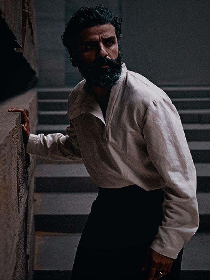 a man with a beard leaning against a wall