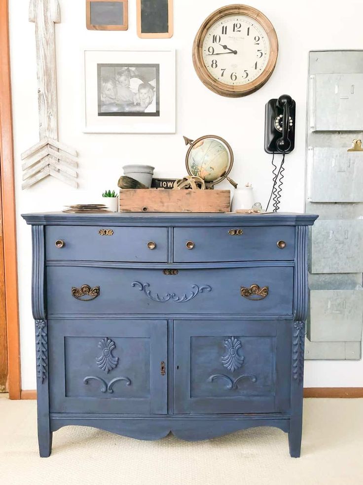 an old dresser painted blue with ornate carvings and knobs on the top, in front of a clock