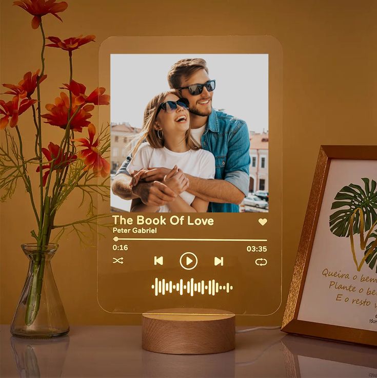 an illuminated photo frame next to a vase with flowers