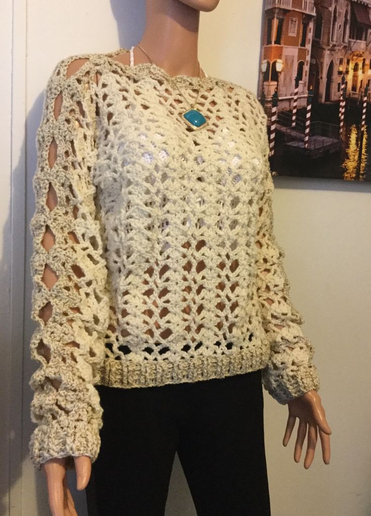 a mannequin wearing a crocheted sweater and black pants in front of a painting