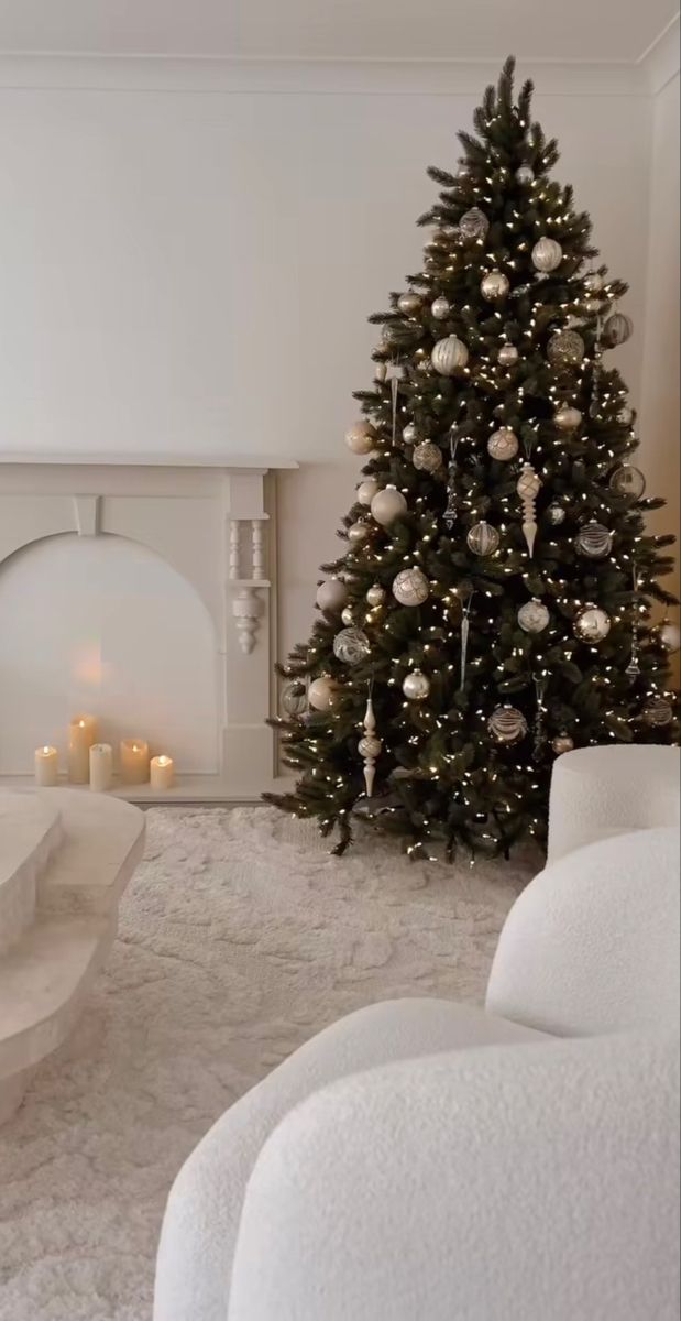 a living room with a christmas tree in the corner and candles on the fireplace mantel