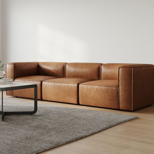 a brown leather couch sitting on top of a wooden floor next to a white wall