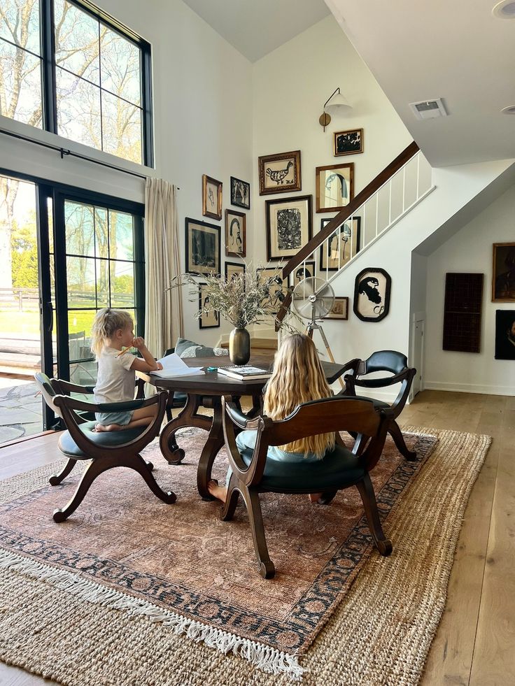 two children sitting at a table in the middle of a room with pictures on the wall