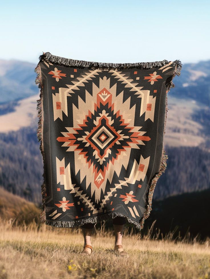 a person standing on top of a hill holding a black and orange blanket over their head