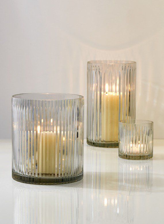 two clear glass candles sitting next to each other on a white counter top with reflections