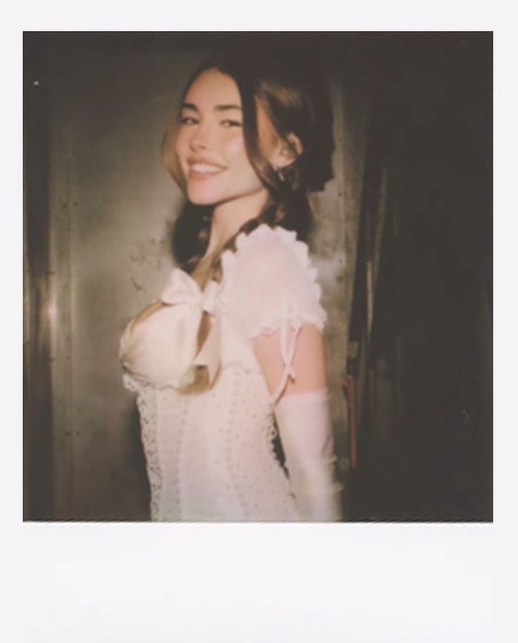 a woman with long hair and white dress posing for a photo in front of a wall