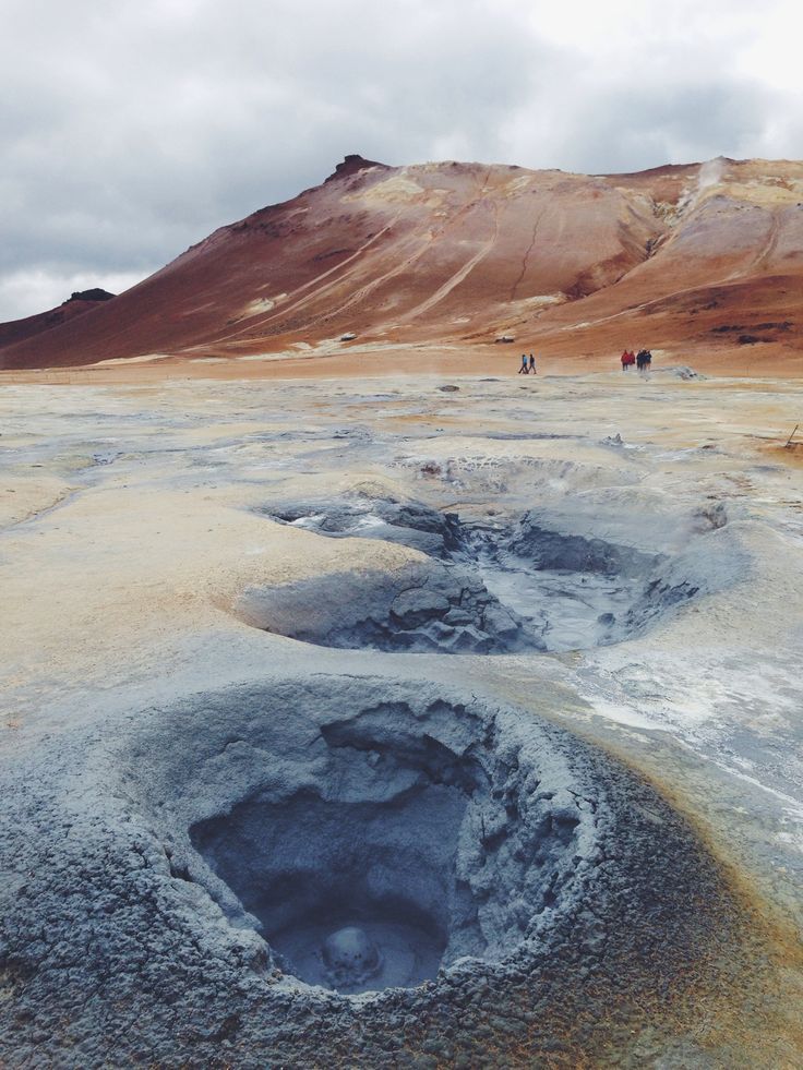 some people are walking in the distance on a barren area with blue water and brown hills