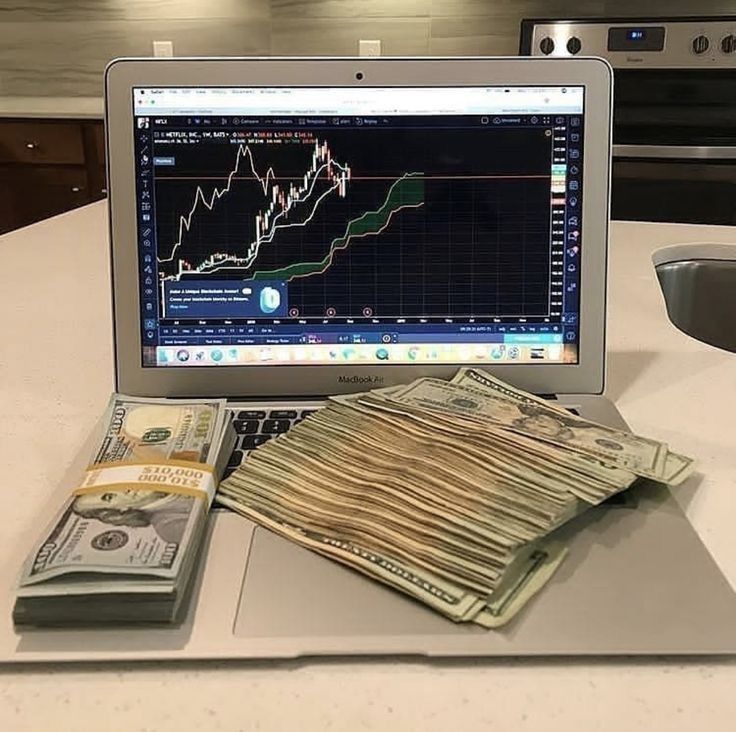 an open laptop computer sitting on top of a table filled with money and stacks of bills