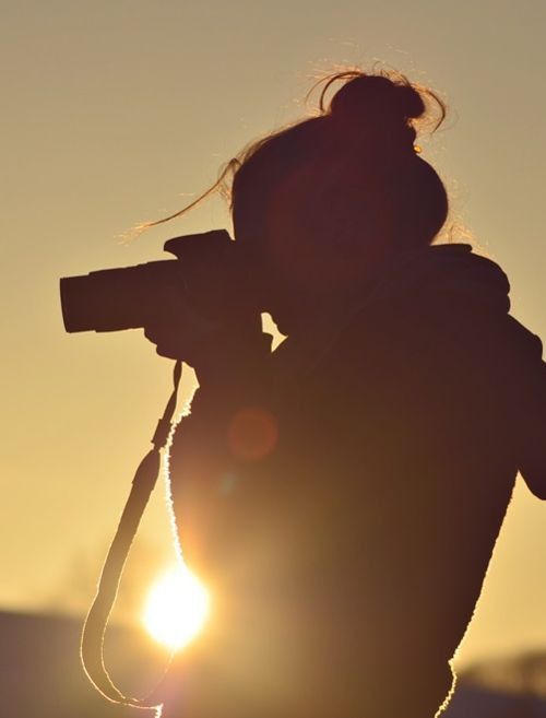 black and white photograph of a person holding a camera in the air with the sun behind them