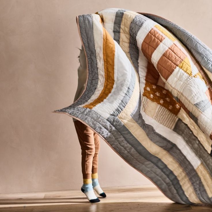 a woman is hiding under a quilt on the floor