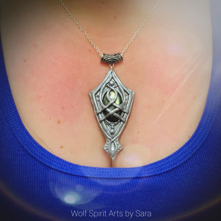 "Vandil, Elvish for \"staff\"! This pendant was inspired by the design of the top of a certain White Wizards' staff from a certain movie about a ring 😉 It's a shield-like design, and the focal stone is a yellow-flash Labradorite that has lots of flash to it! The design flows and crosses the stone, and has been highlighted with silver pigment then sealed with a glaze! To invite this piece into your life is to invite in a little bit of magick! Each piece is a one-of-a-kind that is created with in Fantasy Polymer Clay Jewelry As A Gift, Handmade Polymer Clay Jewelry In Fantasy Style, Handmade Pendant Necklace For Fantasy Events, Hand Painted Silver Jewelry For Crafting, Silver Polymer Clay Pendant Jewelry, Handmade Silver Polymer Clay Jewelry, Polymer Clay Pendant Jewelry For Crafting, Unique Handmade Necklaces For Fantasy Events, Artistic Polymer Clay Jewelry For Crafting