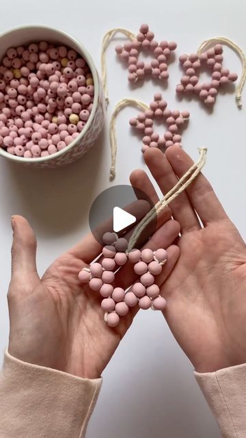 two hands holding pink beads next to a bowl of candy