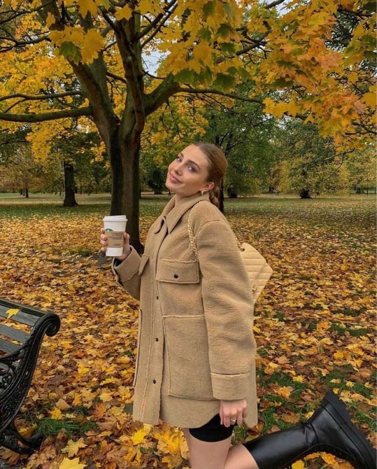 a woman standing next to a park bench holding a cup of coffee