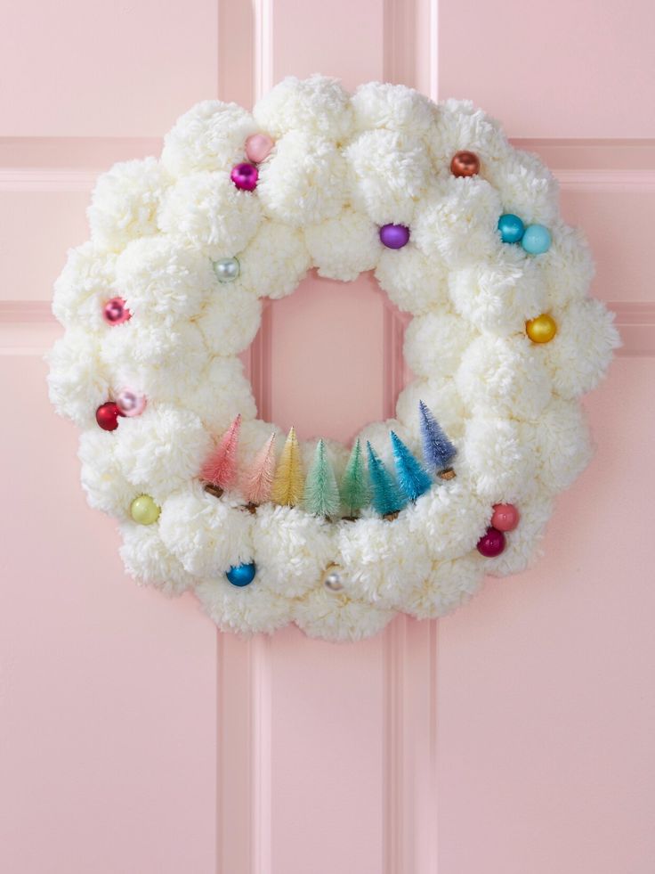 a white wreath with colorful ornaments hanging from the front door, on a pink door