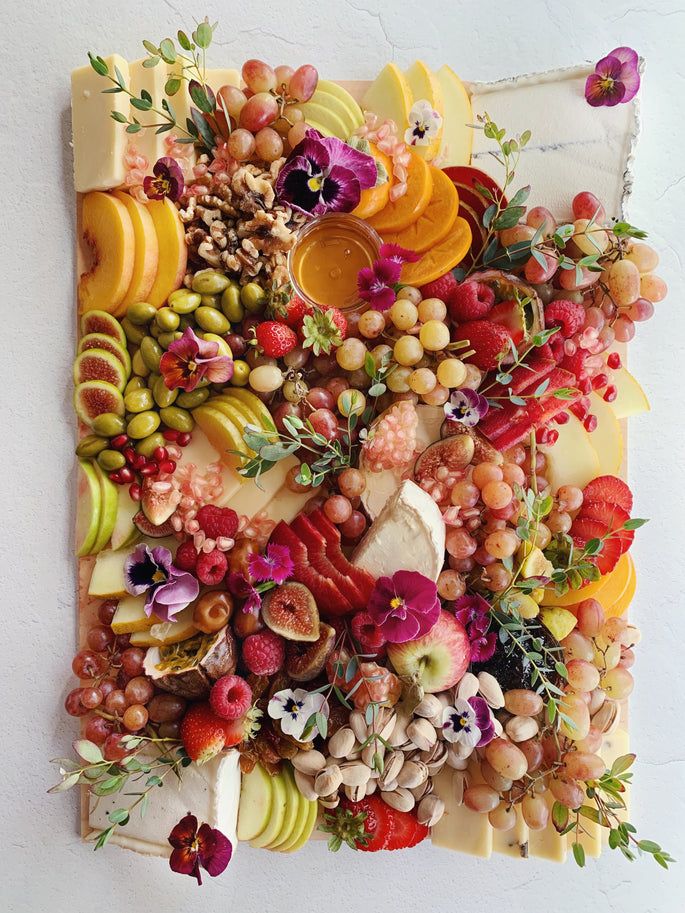 an arrangement of fruits and vegetables is displayed on a white surface with flowers, leaves, and fruit