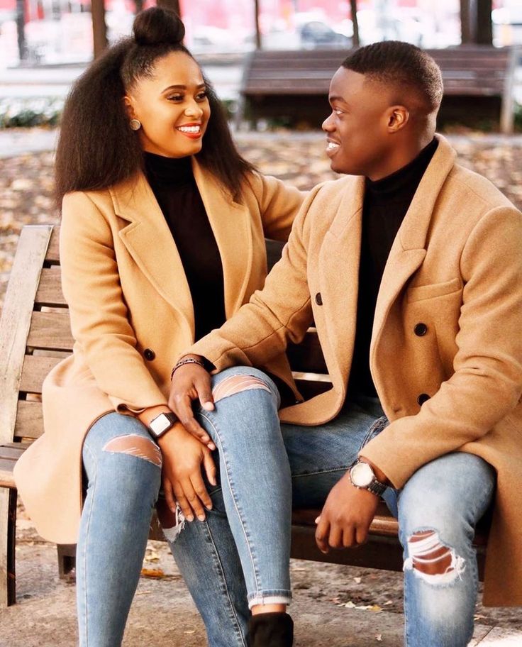 a man and woman sitting on a park bench smiling at each other's eyes