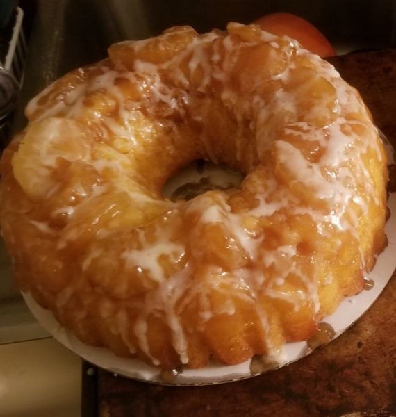 a glazed donut sitting on top of a white plate next to an orange apple