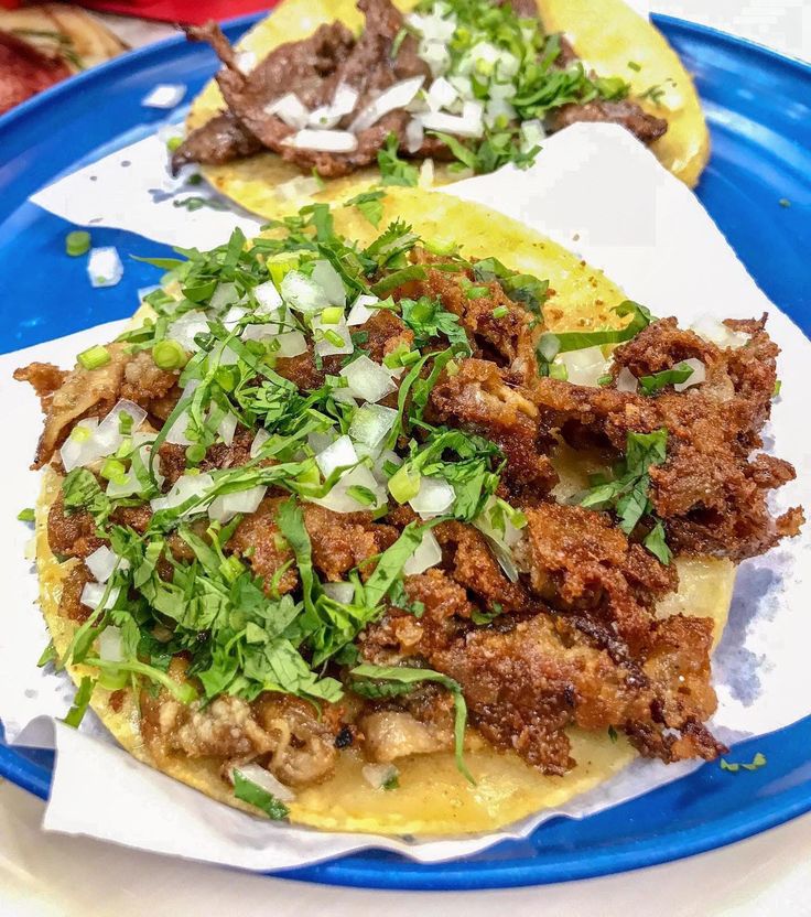 two tacos with meat, onions and cilantro on a blue plate next to other food items