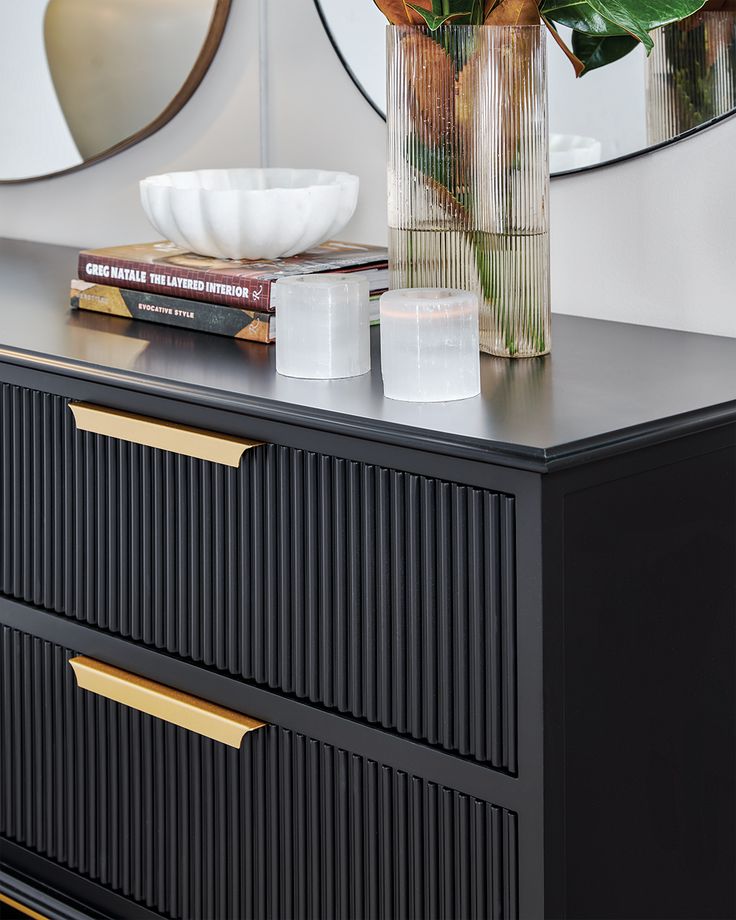 a black dresser topped with a vase filled with flowers