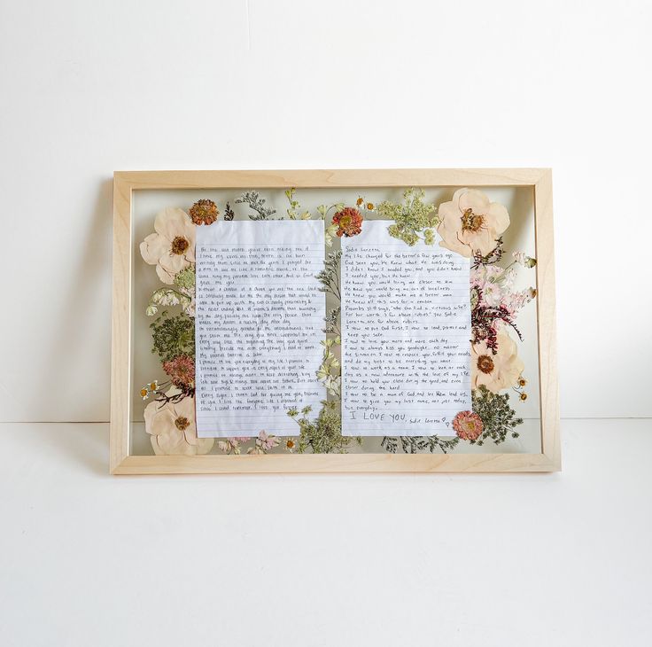 an open book with paper flowers and leaves on it is displayed in a wooden frame