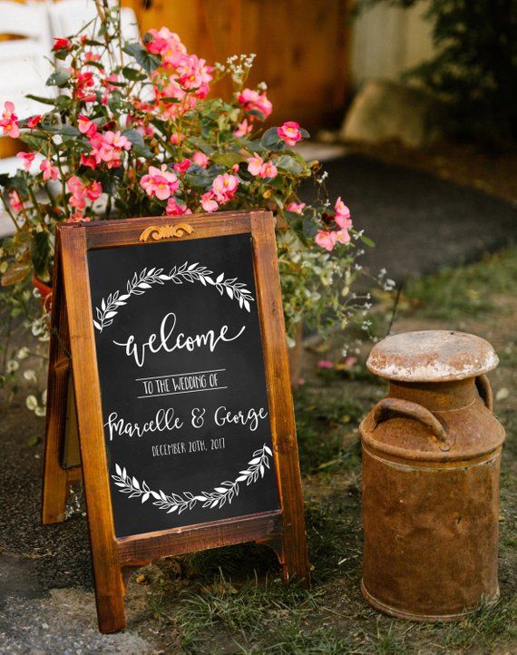 a chalkboard sign sitting next to a potted plant with pink flowers in the background