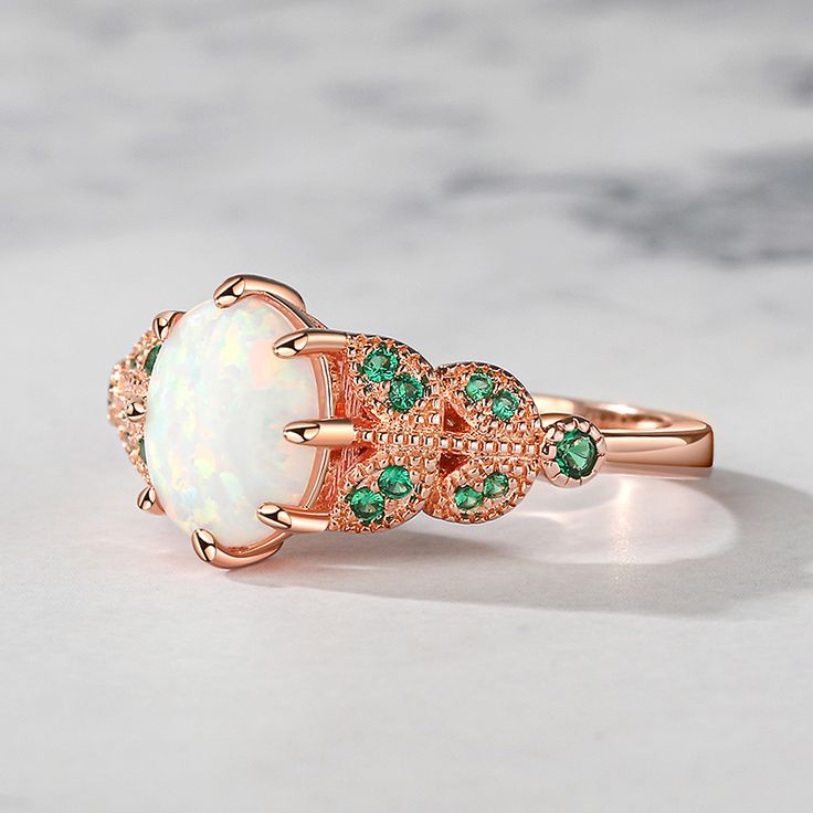 Celebrate your journey of love with the opal engagement ring, a symbol of a love story as rare and beautiful as the gem it holds. Crafted in a captivating rose gold hue, this ring is a true symbol of everlasting beauty. Its graceful band is delicately adorned with exquisite leaf motifs, showcasing nature's enchanting allure. At the heart of this mesmerizing piece lies a magnificent opal, radiating with iridescent hues that capture the essence of a thousand sunsets. Its ethereal glow is complemented by the subtle sparkle of vibrant green stones, reminiscent of lush emerald gardens.Carat Weight: 0.136 ctStone Size: 1.6,0.9,1.1 mmStone Type: Jeulia® StoneNumber of Stones: 18 Stone Shape: RoundStone Color: Emerald GreenWeight: 2.5 gWidth: 2 mmHeight: 5.4 mmThickness: 1.2 mmMaterial: 925 Silver Luxury Rose Gold Opal Gemstone Ring, Luxury Rose Gold Opal Ring, Rose Gold Opal Ring Fine Jewelry, Fine Jewelry Opal Promise Ring, Elegant Opal Ring With Center Stone, Rose Gold Opal Birthstone Ring As Gift, Rose Gold Opal Birthstone Ring For Gift, Elegant Opal Cabochon Promise Ring, Rose Gold Oval Opal Promise Ring