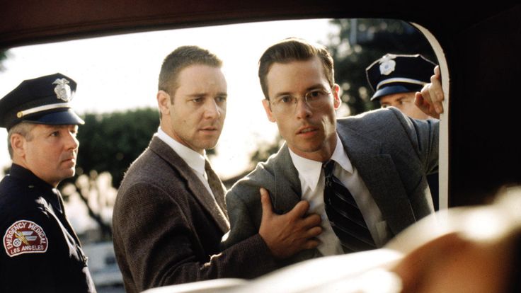 two men in suits and ties standing next to each other with one pointing at the camera