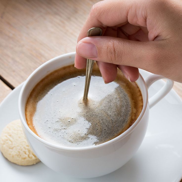 a person dipping sugar into a cup of coffee