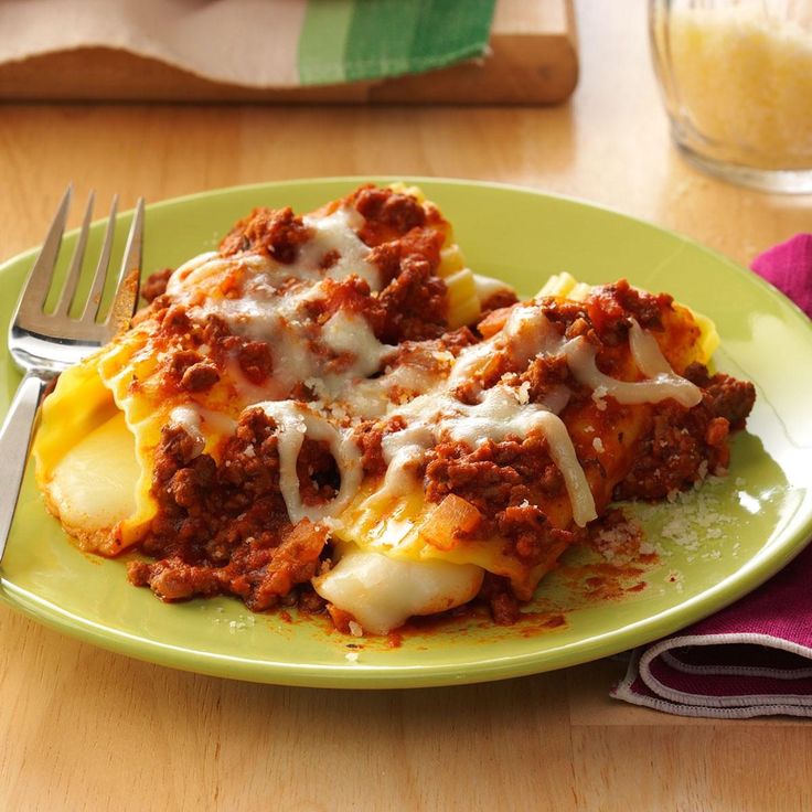 a green plate topped with lasagna covered in cheese and sauce next to a fork