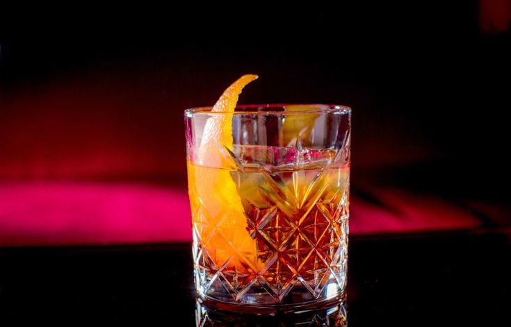 a close up of a drink in a glass with an orange peel on the rim