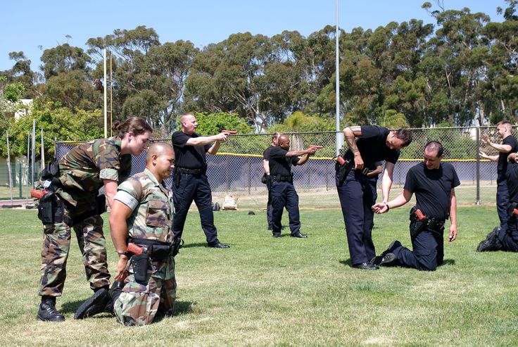 some men in uniform are playing frisbee on the grass and one man is kneeling down