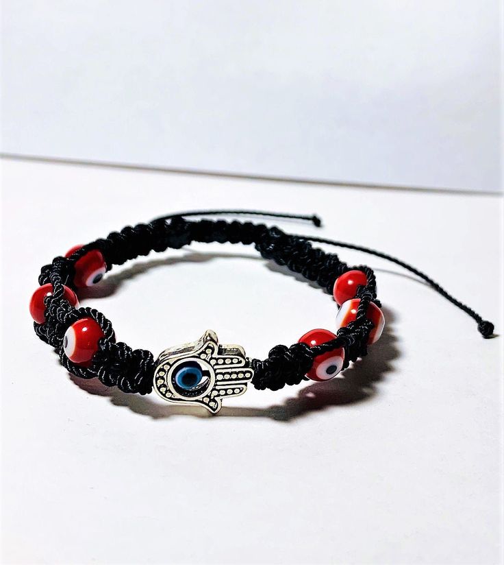 Carefully hand braided bracelet with charms that work as negativity shields. It is made with strong Black nylon thread and vibrant red evil eye beads ( represent courage and protection). The Hamsa hand is also a charm of protection and fortune caller as you can see it comes with a 2 mm evil eye in the middle (color blue, is the traditional color for good karma, positive energies, and protection against the evil eye.) When is finally made, the bracelet is then aligned with the wearer's name, an a