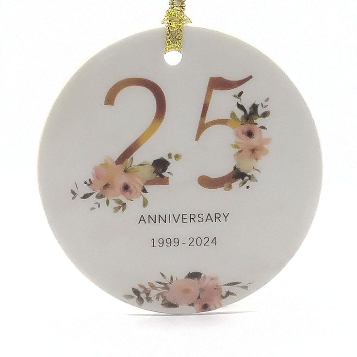 the 25th anniversary ornament is decorated with pink flowers and gold lettering on a white background