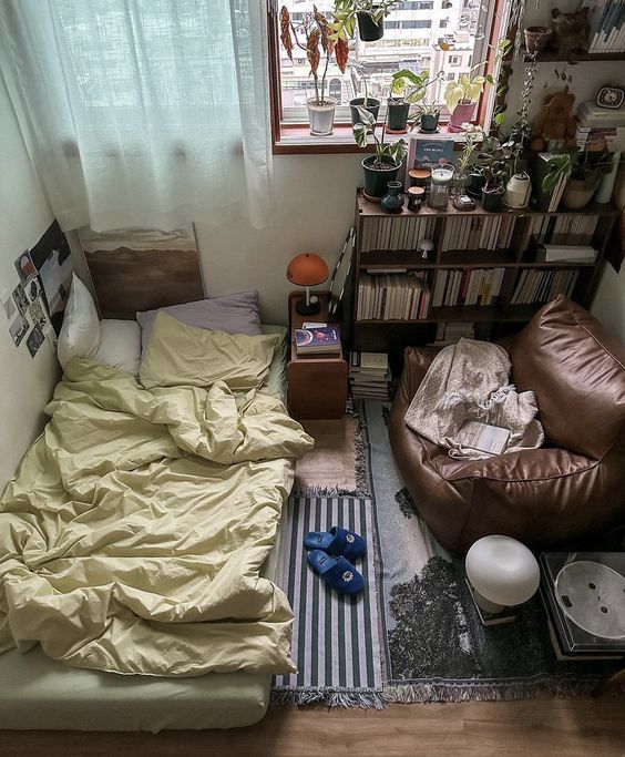 a small room with a bed, couch and bookshelf on the floor in front of a window