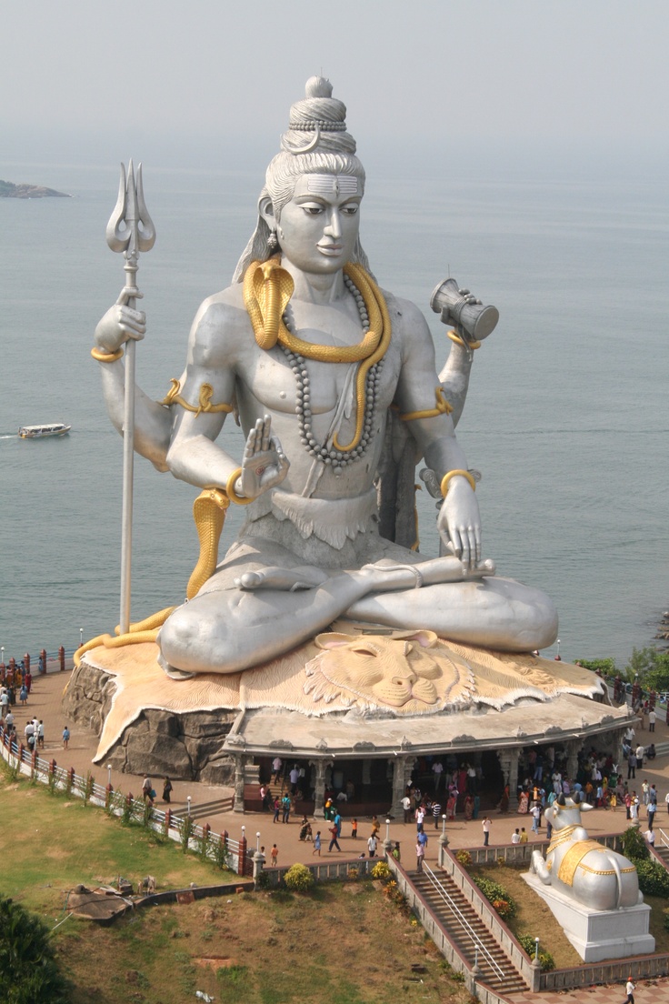 a large white statue sitting on top of a lush green field next to the ocean