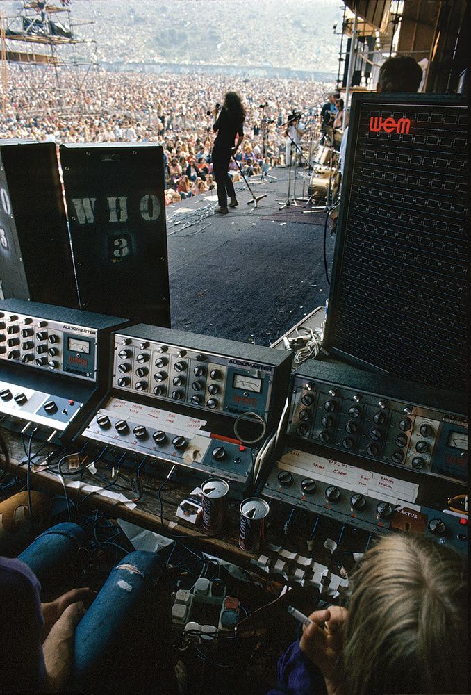 a man standing in the middle of a stage surrounded by sound equipment and people watching